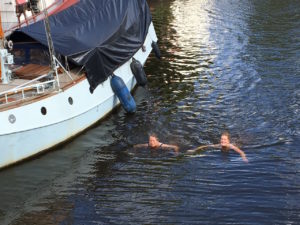 Boats and swimmers share a canal.  The swimmers are diligent about keeping their head above water!